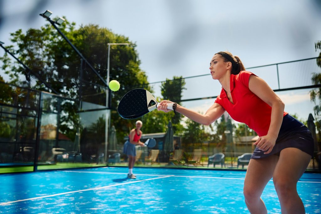 Female paddle tennis player hitting the ball during doubles match on outdoor court.